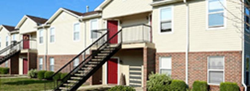 Two story brick apartment with a black staircase leading up to a landing, and red doors.